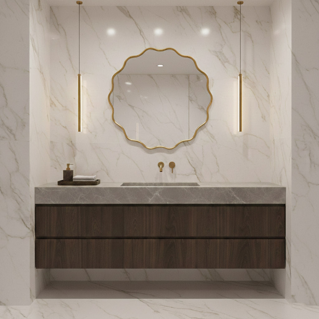 Round wavy brass mirror above dark wood vanity in marble bathroom.