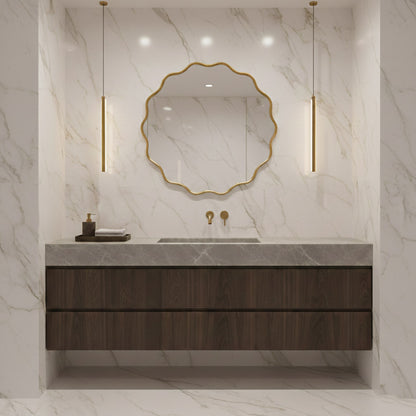 Round wavy brass mirror above dark wood vanity in marble bathroom.