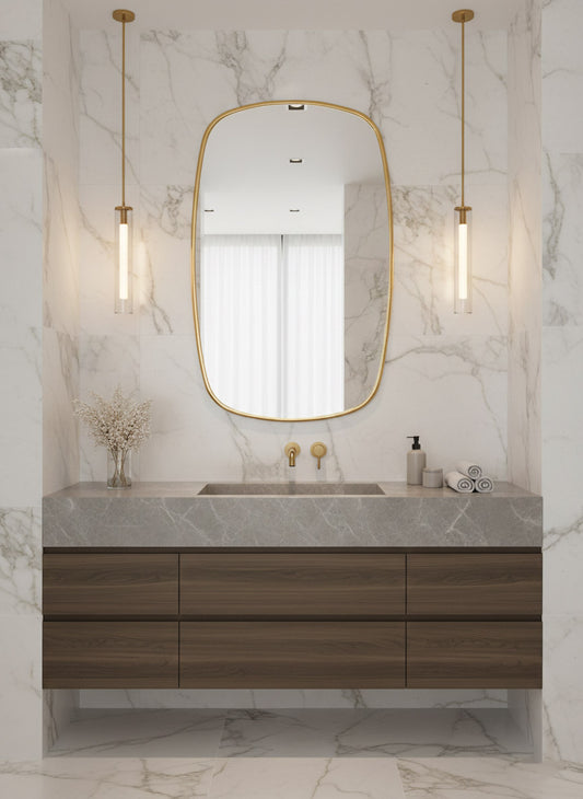 Brass mirror centered above wood vanity in marble bathroom