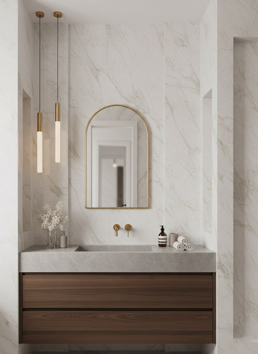 Arched brass vanity mirror in white marble bathroom