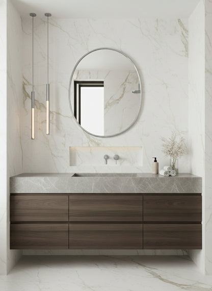 Silver brass oval mirror over wood floating vanity in marble bathroom.