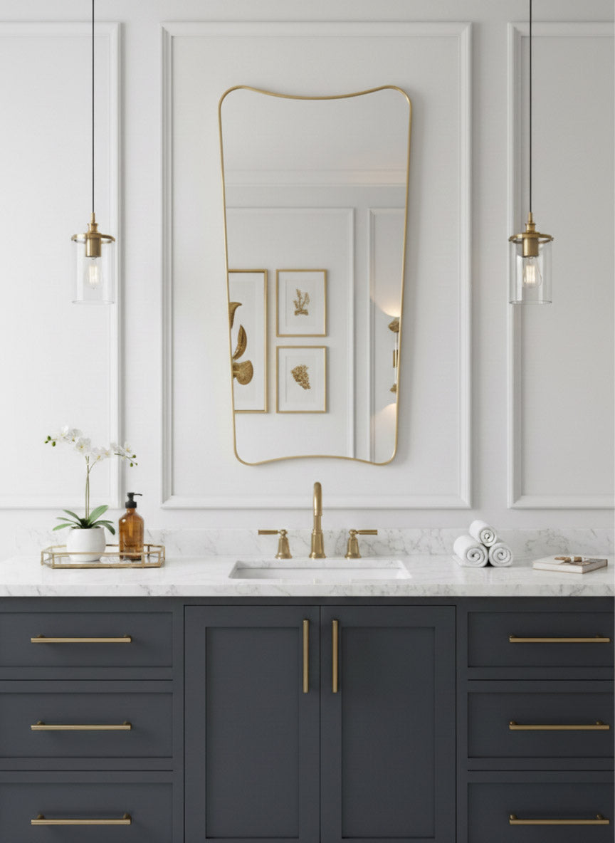 Brass wall mirror above bathroom vanity with white paneling and gold fixtures