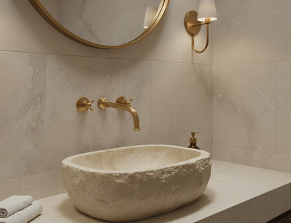 Oval stone sink with brushed brass wall faucet and round mirror