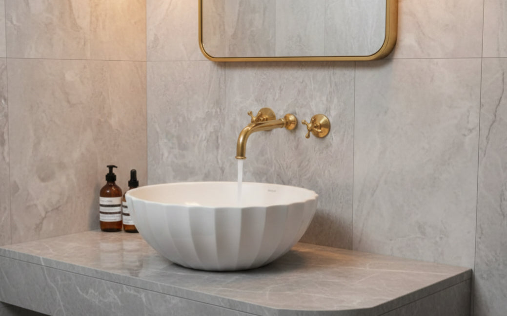 White fluted vessel sink with wall-mounted brass faucet and mirror