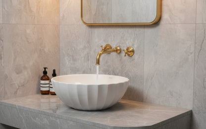 White fluted vessel sink with wall-mounted brass faucet and mirror