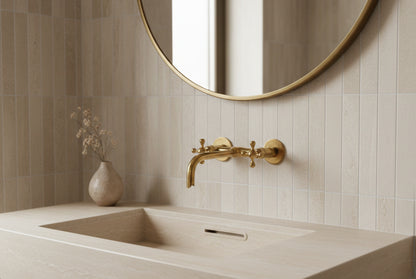 Brass wall faucet above integrated stone sink with round brass mirror.