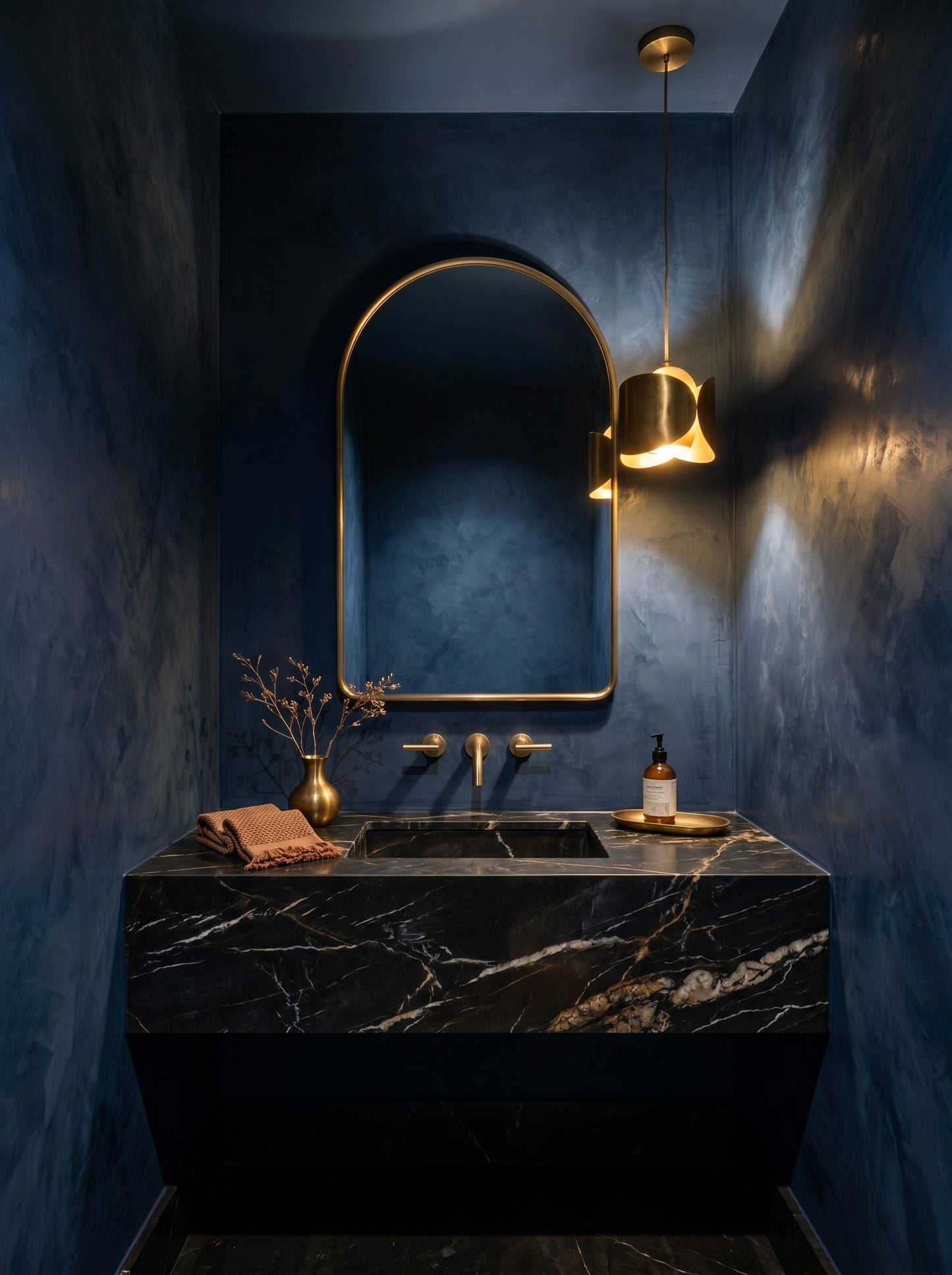 Moody navy powder room with arch brass mirror and black marble vanity