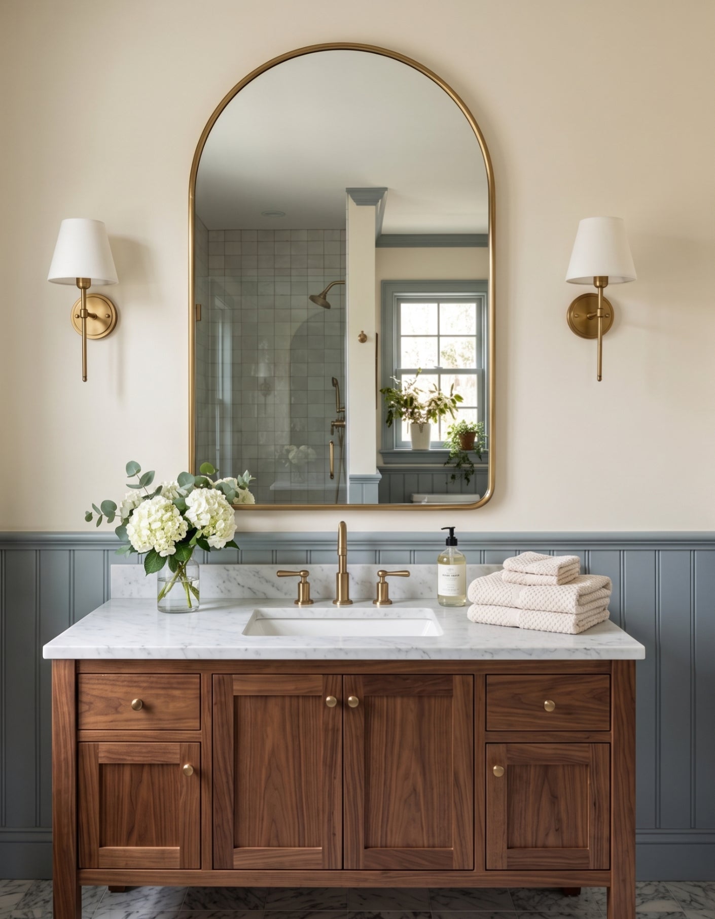 Arched brass mirror above walnut bathroom vanity with marble countertop