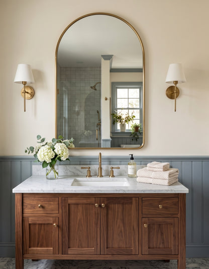 Arched brass mirror above walnut bathroom vanity with marble countertop