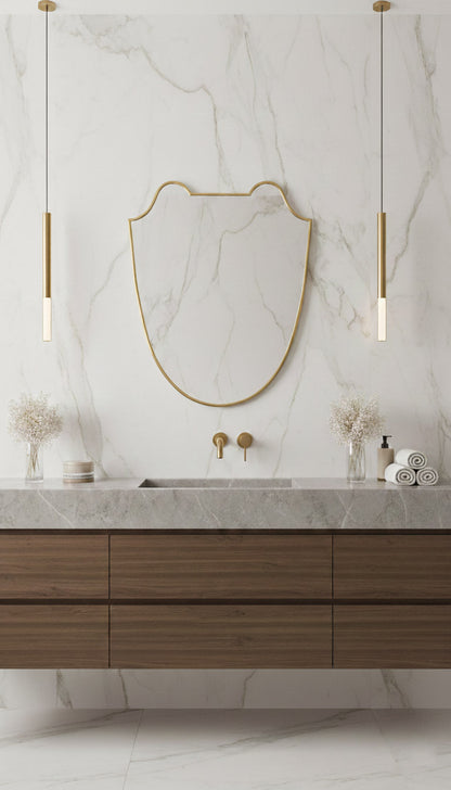 Antique brass shield mirror over marble vanity with pendant lights.
