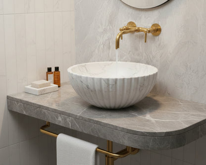 Fluted marble bowl sink with brass wall faucet on stone vanity.