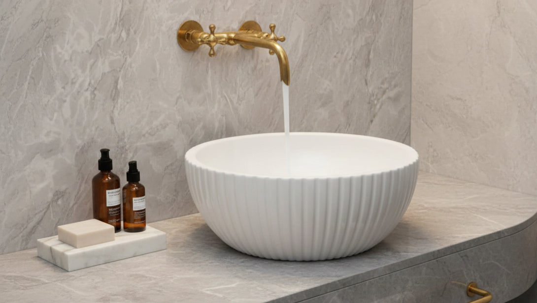 Brushed brass wall faucet over white ribbed vessel sink on marble vanity.