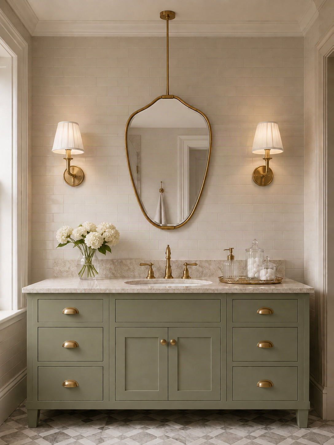 A styled bathroom vanity featuring a sage green cabinet with brass hardware, a white marble countertop, a central sink, a gold-framed mirror, and matching wall sconces.