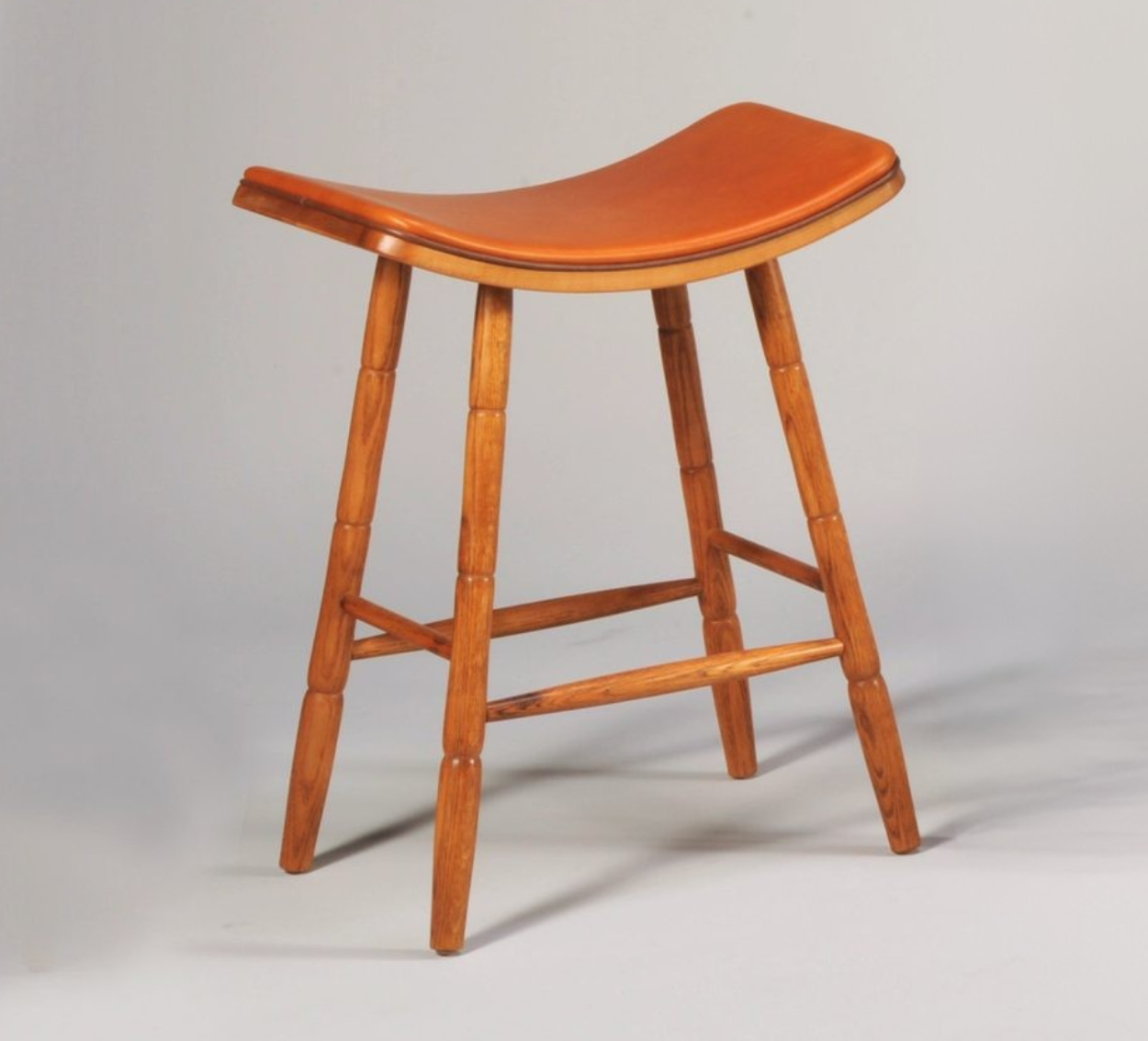 Wooden stool with curved seat on a gray background