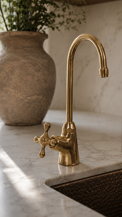 A polished brass kitchen faucet with a high-arc spout and cross handle, installed on a white marble countertop in a modern kitchen setting.