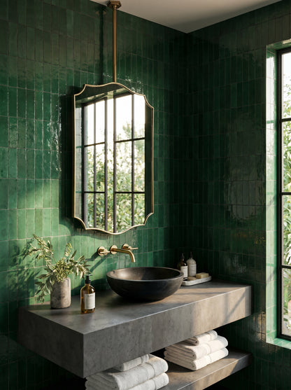 Suspended crest brass mirror above a floating concrete vanity with emerald green zellige tiles and a black vessel sink.