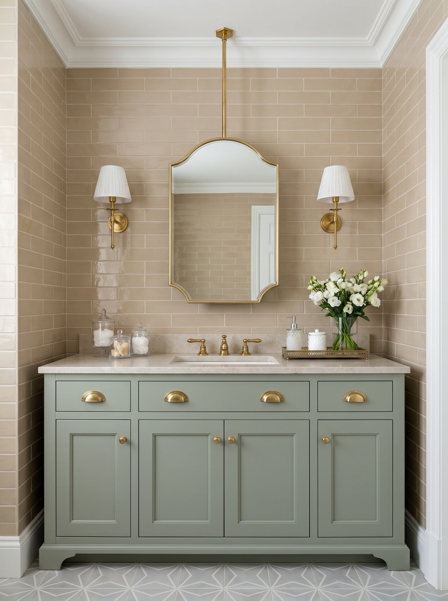 Suspended oval brass mirror above a sage green vanity with brass sconces and beige subway tile bathroom walls.