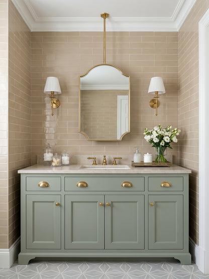 Suspended oval brass mirror above a sage green vanity with brass sconces and beige subway tile bathroom walls.