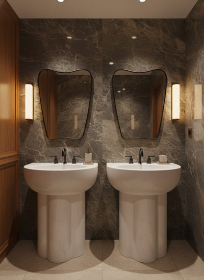 Set of organic black mirrors above pedestal sinks in marble bathroom.
