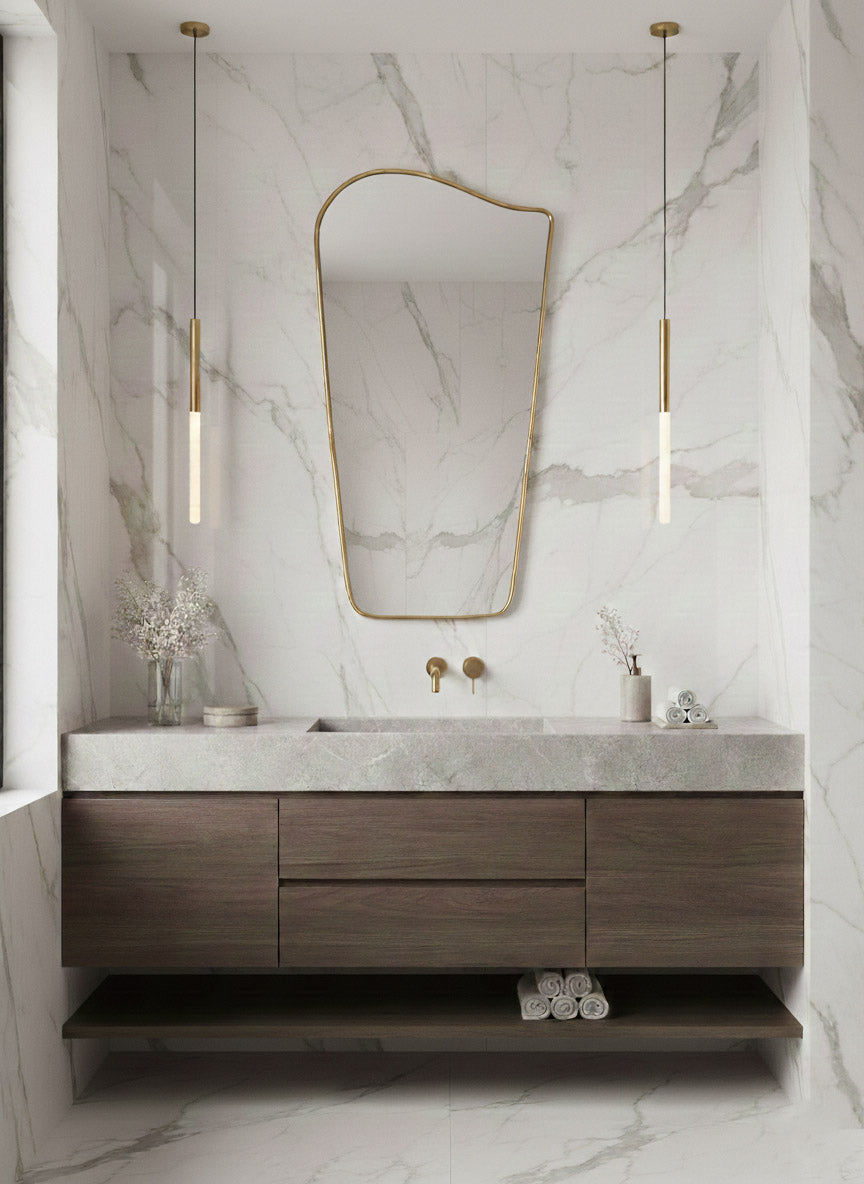 Wave brass mirror centered above wood vanity in marble bathroom
