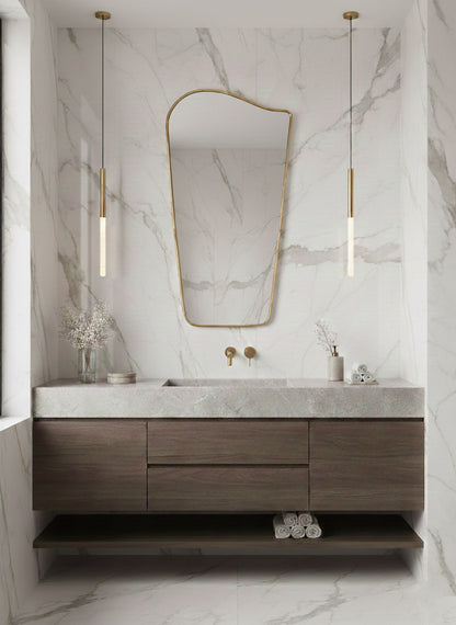 Wave brass mirror centered above wood vanity in marble bathroom