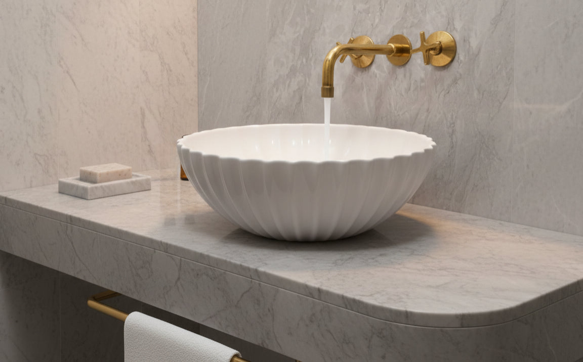 White fluted bowl sink on marble countertop with brushed brass wall faucet.