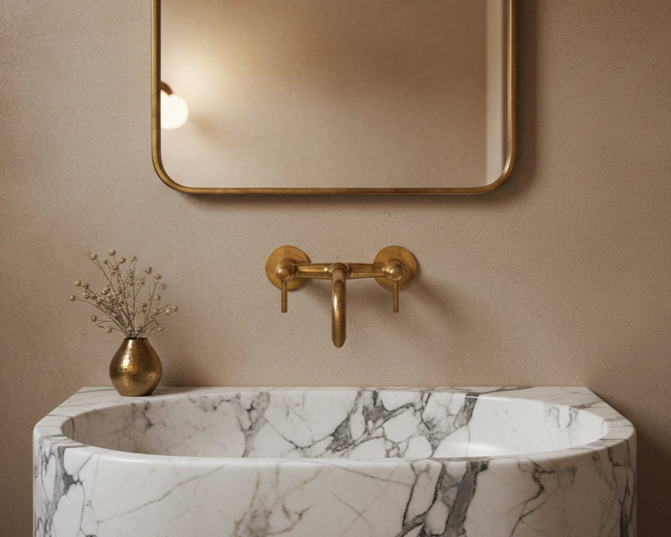 Marble basin with warm brass wall faucet under minimalist brass mirror.