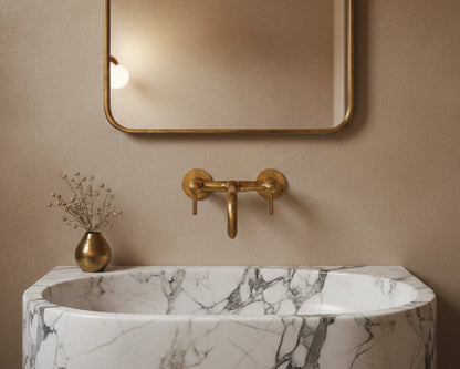 Marble basin with warm brass wall faucet under minimalist brass mirror.