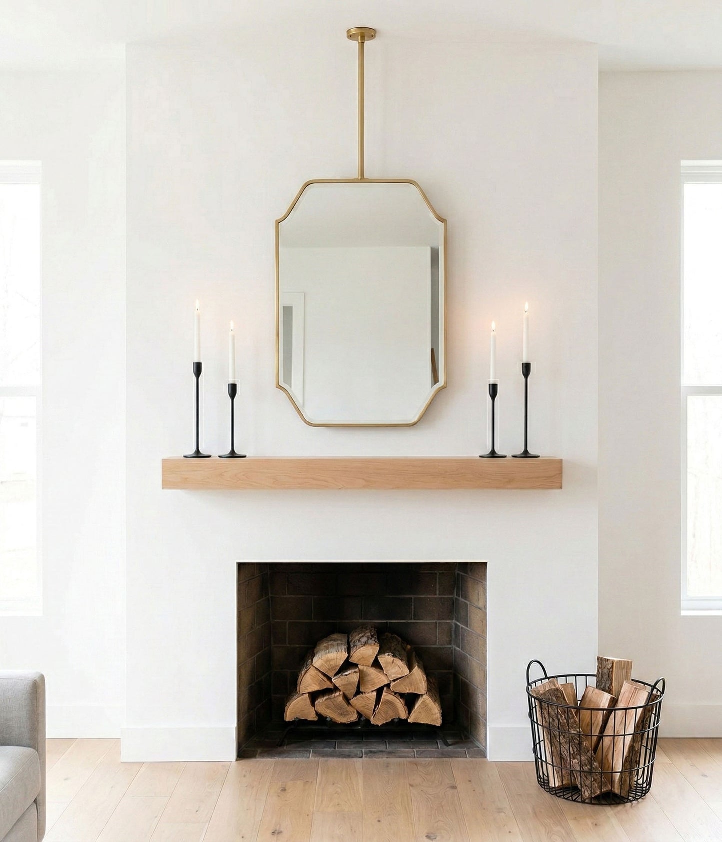 Suspended brass mirror above fireplace mantel with minimalist decor and candles.