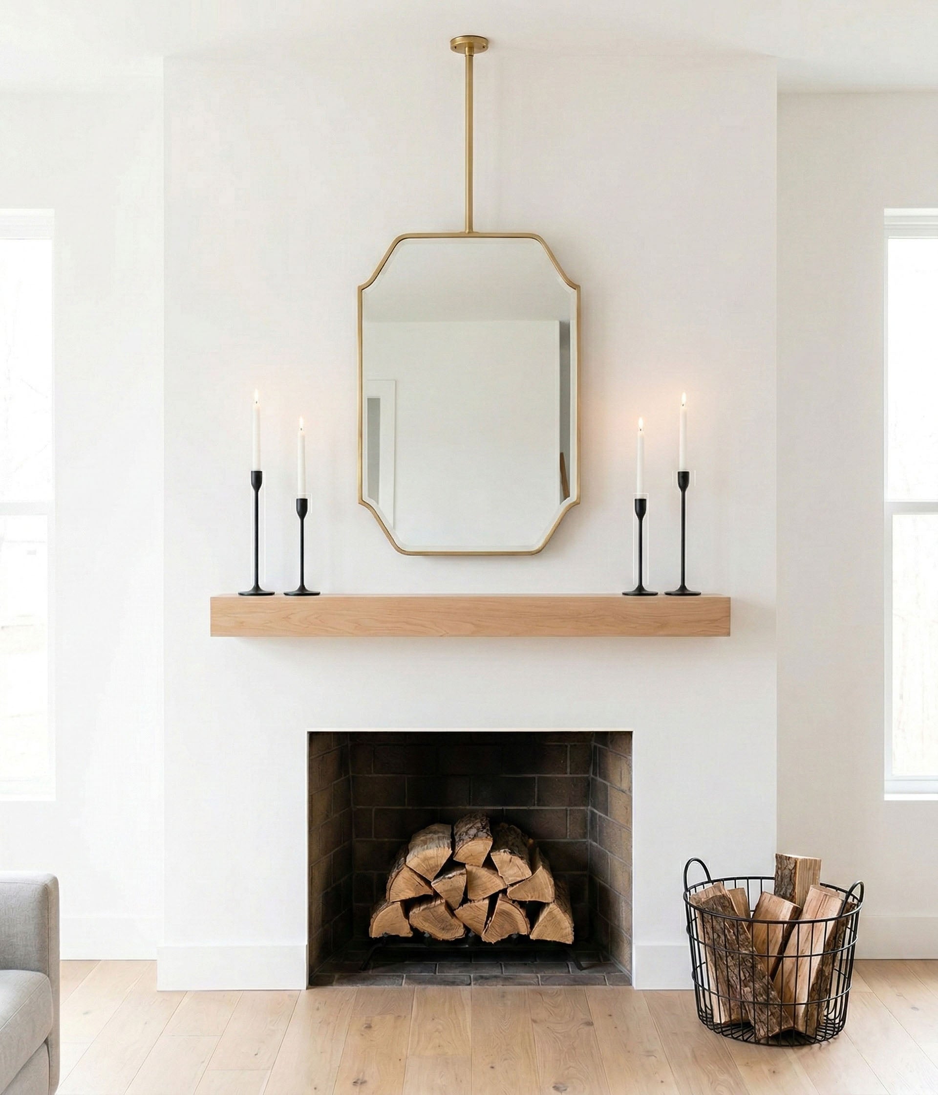 Suspended brass mirror above fireplace mantel with minimalist decor and candles.