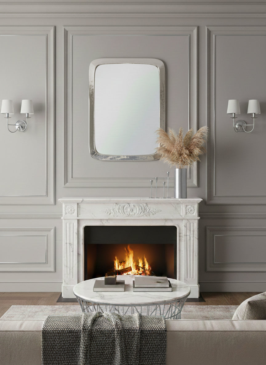 Silver rounded rectangle mirror above a classic white marble fireplace.
