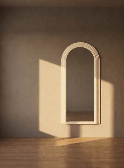 An arched, ribbed wooden mirror frame mounted on a textured beige wall, casting a shadow on a light wood floor with warm sunlight streaming in.