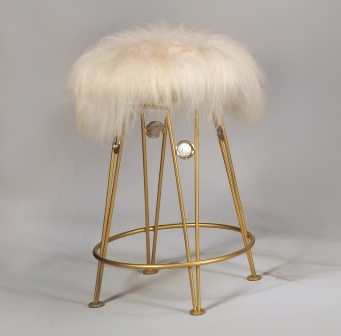 Gold bar stool with a fluffy white cushion on a gray background