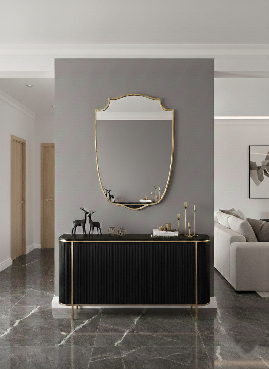 Brass shield mirror above black console table.
