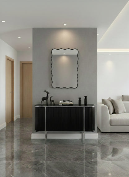 Black brass wall mirror above console table in minimalist entryway.