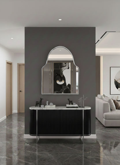 Silver brass wall mirror above black console in modern entryway.