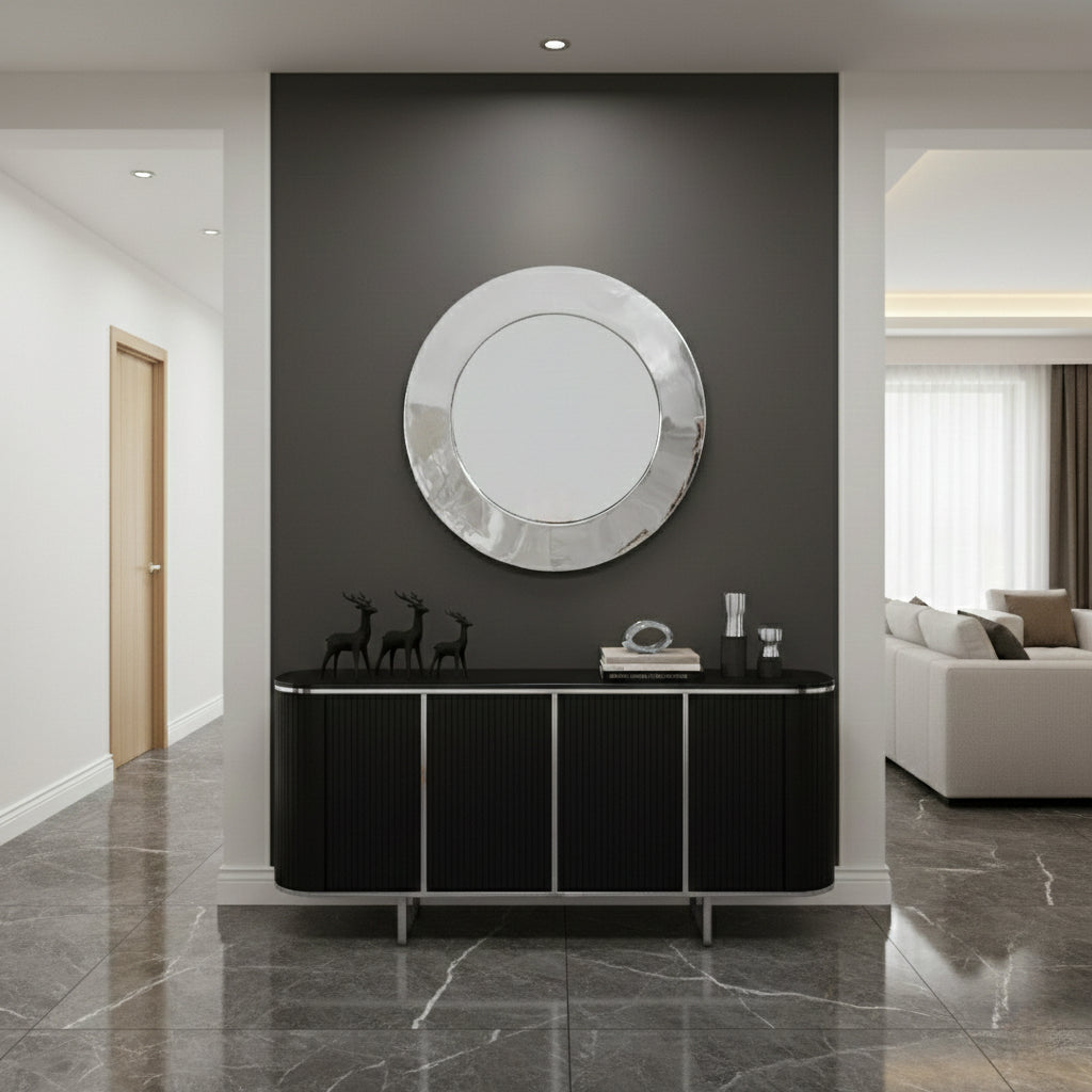 Round silver brass mirror mounted above black console in modern entryway.
