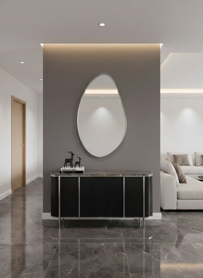 Silver asymmetrical brass mirror above black console.