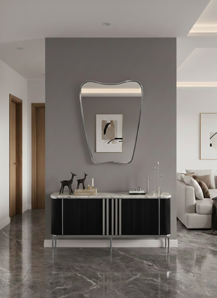 Modern brass mirror above black console table in minimalist entryway.