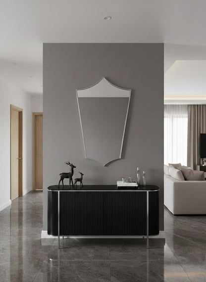 Contemporary shield mirror above black console in a minimalist hallway.