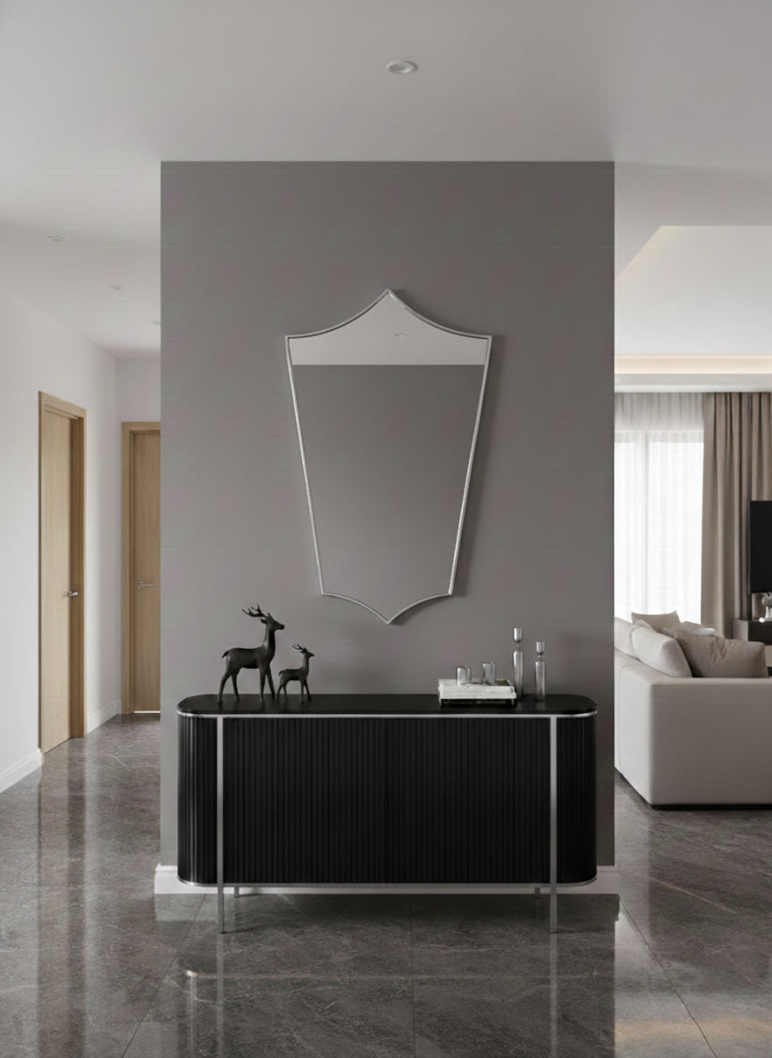 Silver brass shield mirror mounted above black console in modern entryway.