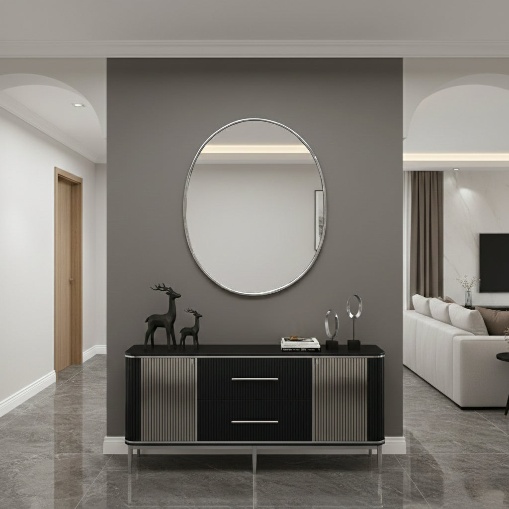 Silver brass oval mirror mounted above black console in modern entryway.