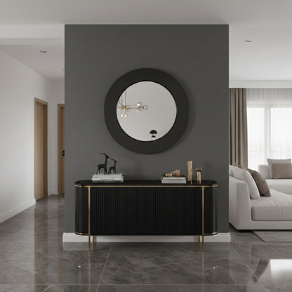 Round brass framed mirror above black console table in modern hallway.