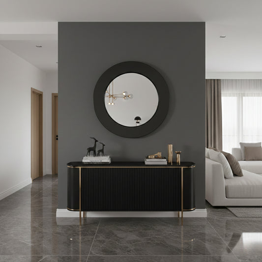 Round brass framed mirror above black console table in modern hallway.