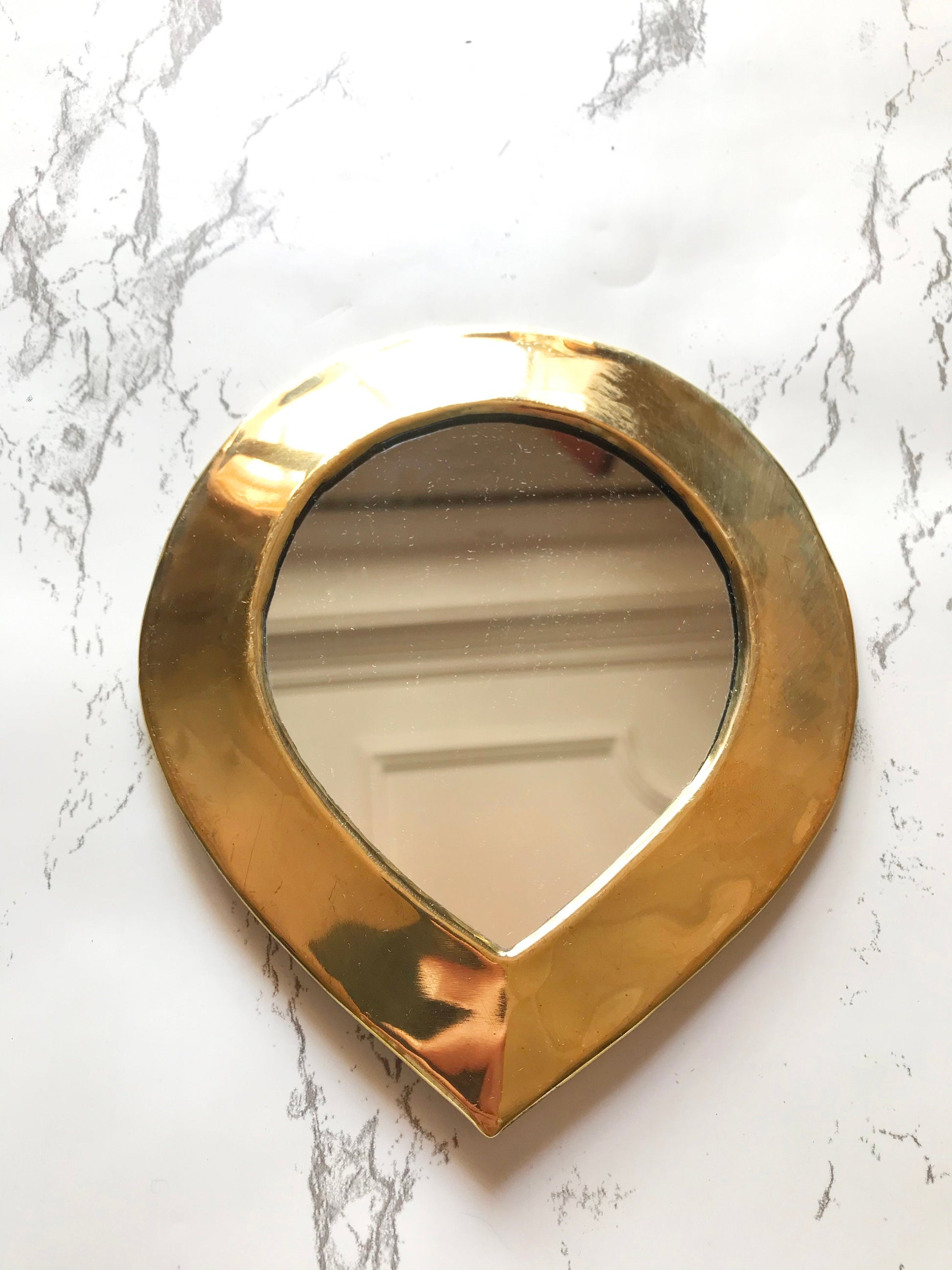 a gold heart shaped mirror on a marble counter