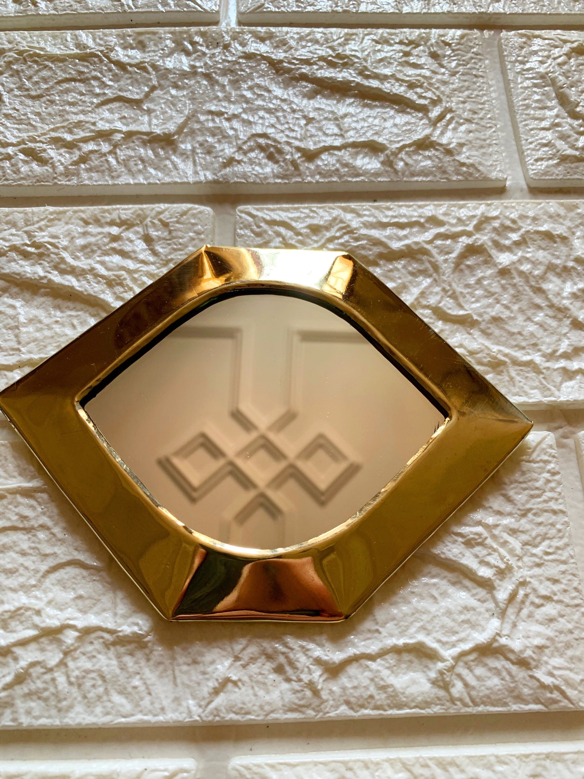 a mirror mounted to a brick wall with a gold frame