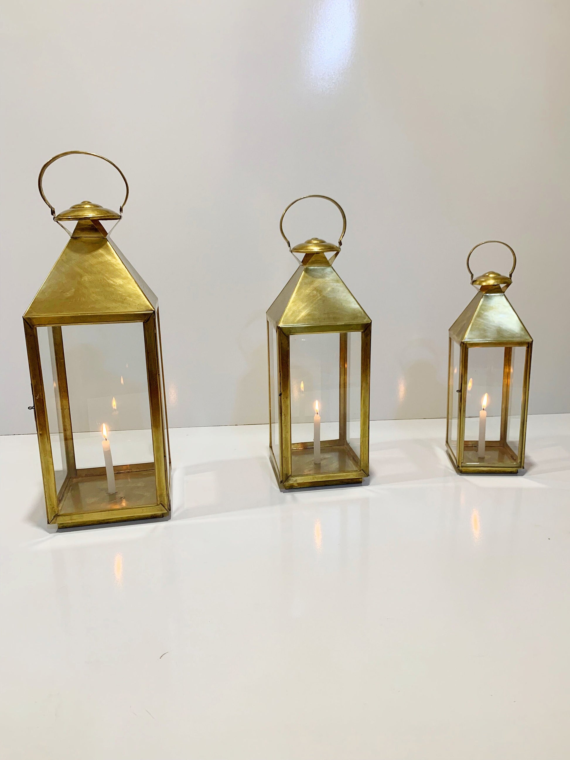 three brass lanterns with lit candles on a white surface