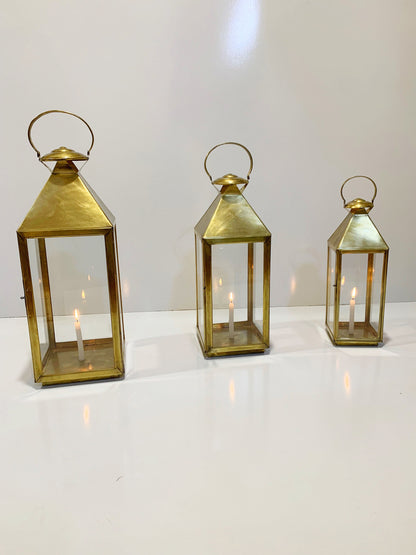 three brass lanterns with lit candles on a white surface