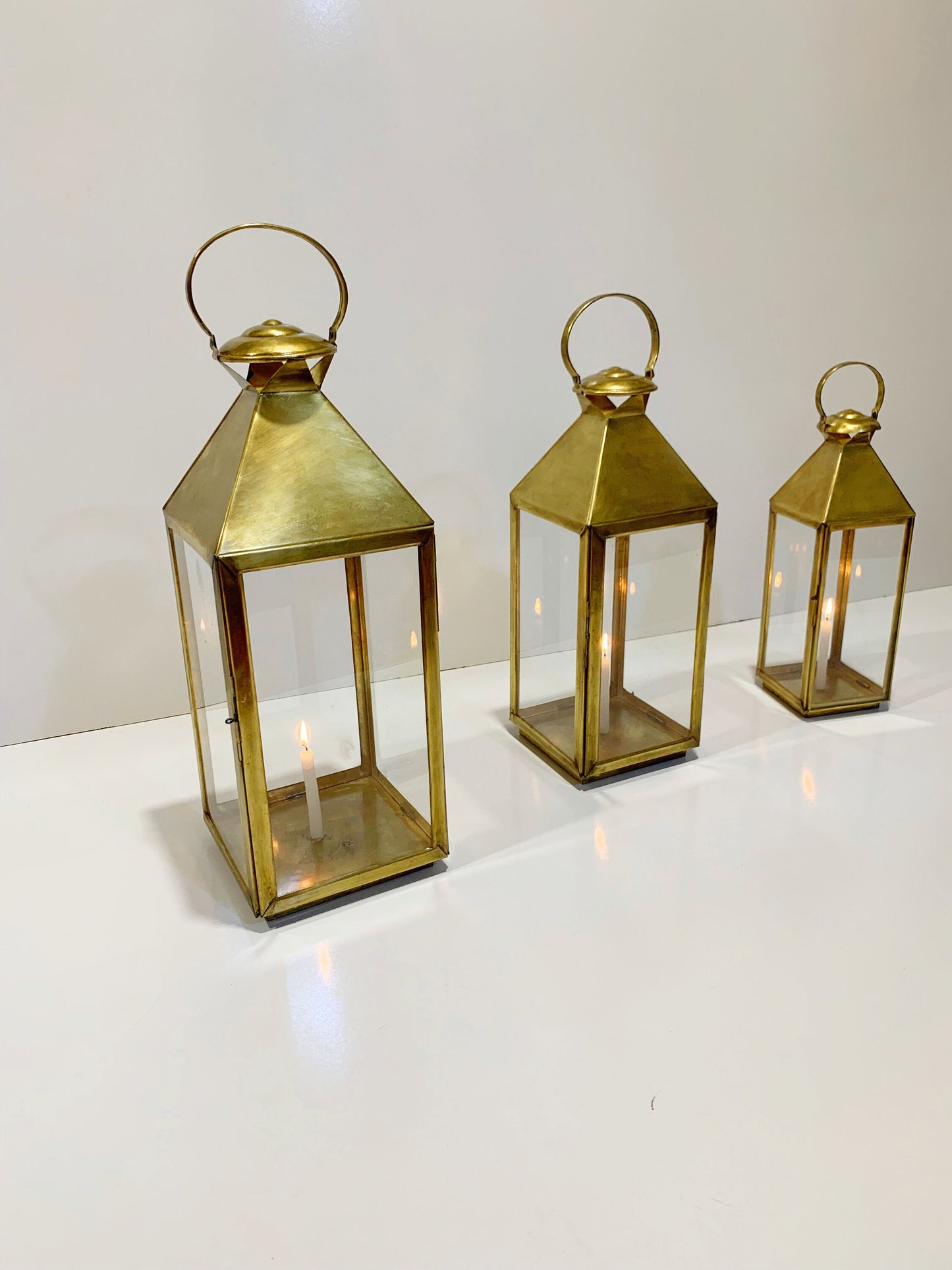 three brass colored lanterns on a white surface