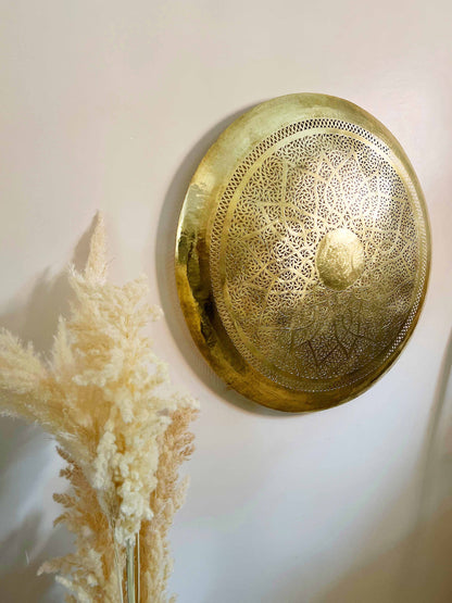 a gold plate sitting on a wall next to a dried plant